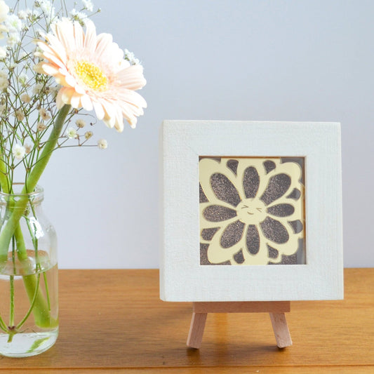 A cute gold mirror acrylic laser cut smiling happy flower, with a gold glitter background, in a rustic white wooden box frame. This design is Daisy Doo.