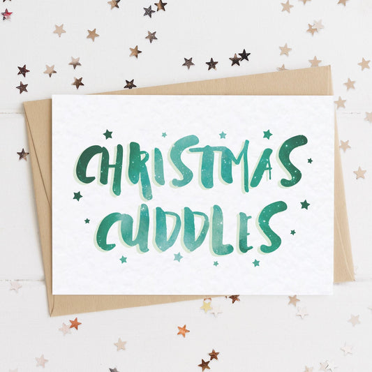 A celestial Christmas card with a stars and text in colours inspired by the northern lights/hygge and the message, "CHRISTMAS CUDDLES".