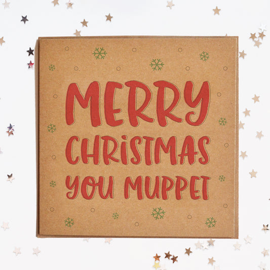 A funny Christmas card in festive colours and the message "Merry Christmas You Muppet" surrounded by decorative snowflakes.