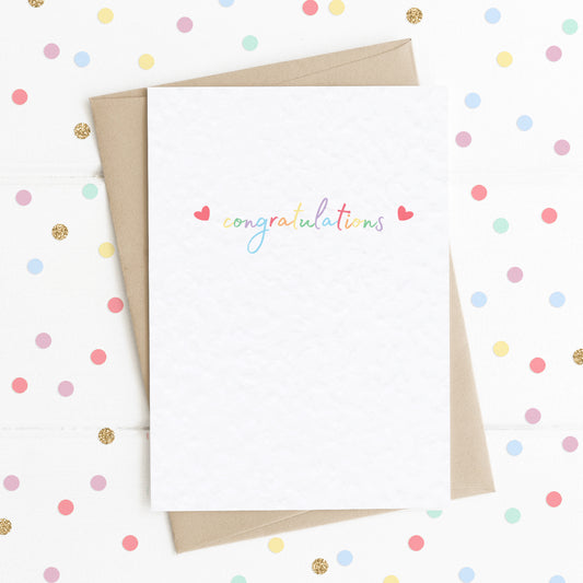 A cute A6 celebration card with the message "Congratulations" in colourful rainbow type, with two reds hearts either side.